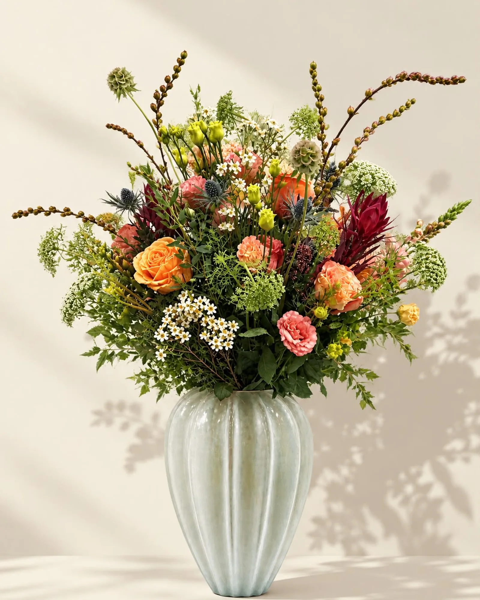 Autumn Glow — burnt-orange roses, leucadendron, scabious seed heads and ammi in a fluted celadon vase, on warm linen